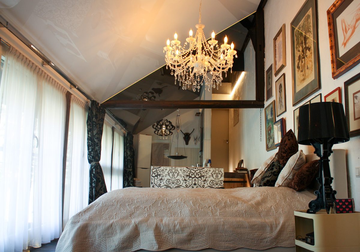 Schlafzimmer mit Hochglanz-Spanndecke und Kronleuchter unter dem Dach