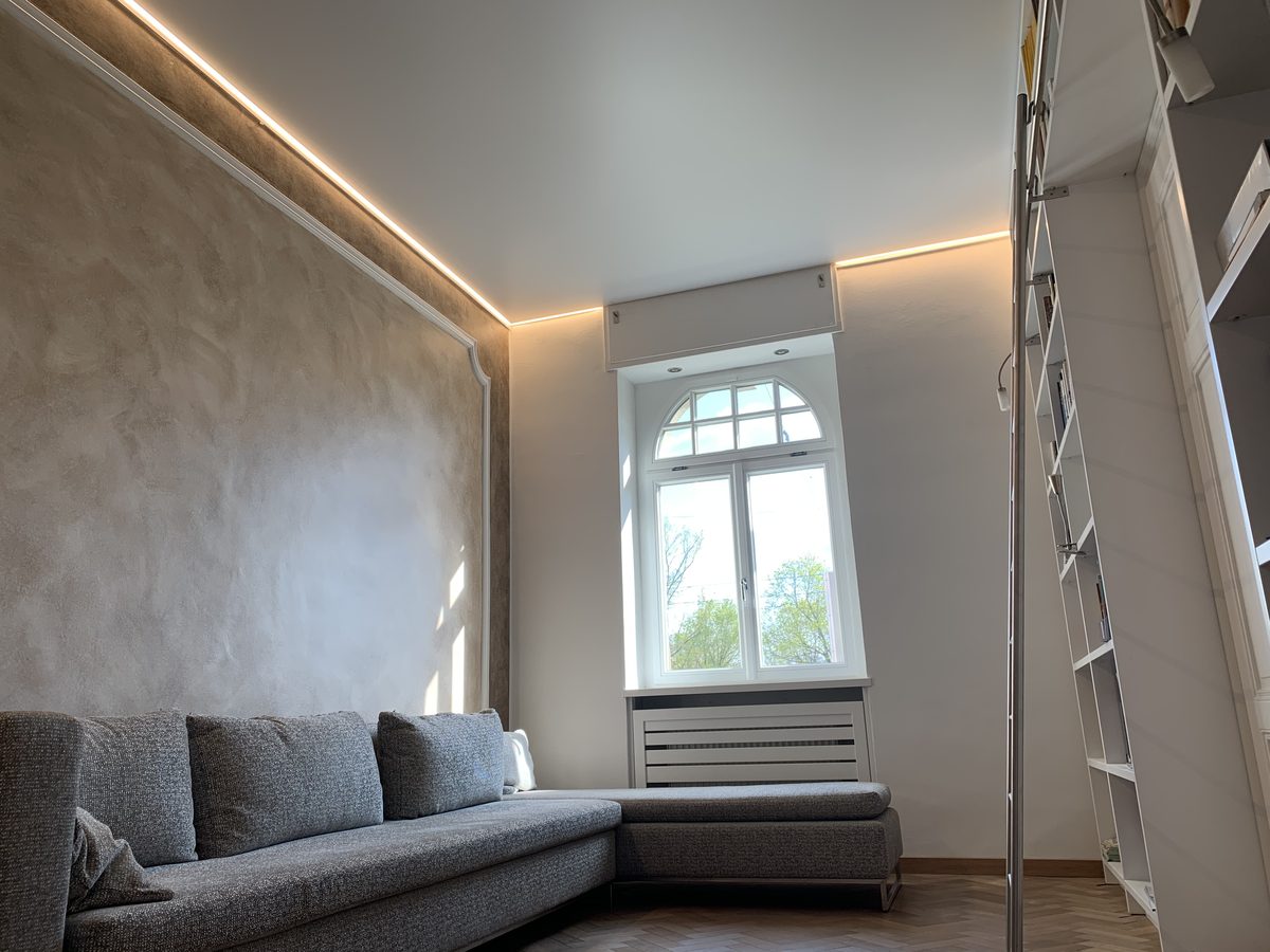 Wohnraum im Altbau mit Spanndecke und Lichtlinie über einer Wand in Betonoptik