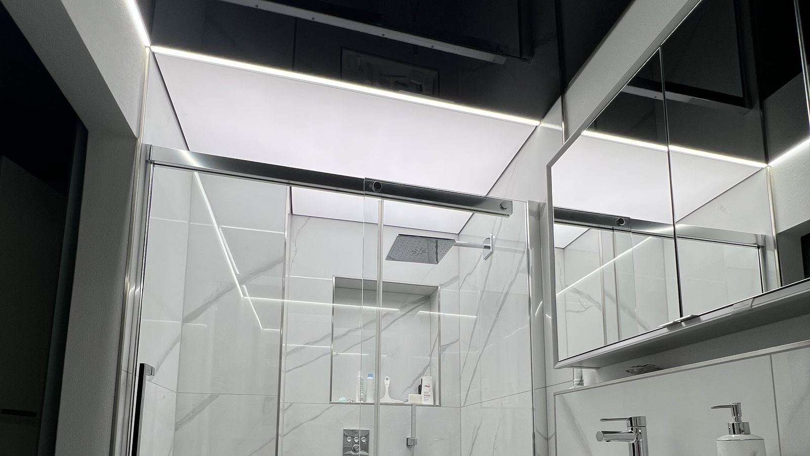 Designbad mit schwarzer Hochglanz-Spanndecke und Lichtlinie über der Dusche